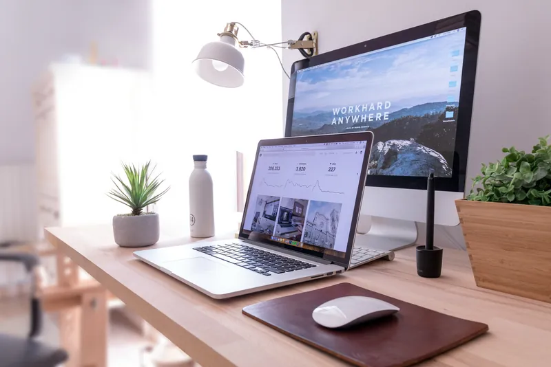 Een bureau met een laptop en een groot scherm waarop een website openstaat