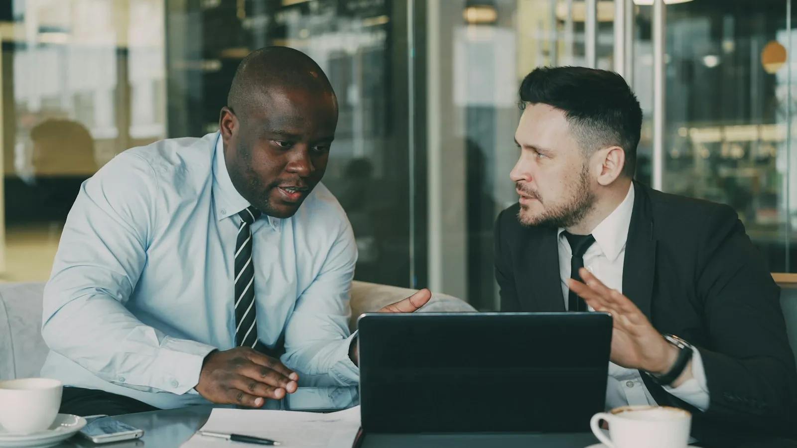Twee mannen in overhemd en pak bespreken iets aan tafel bij een laptop